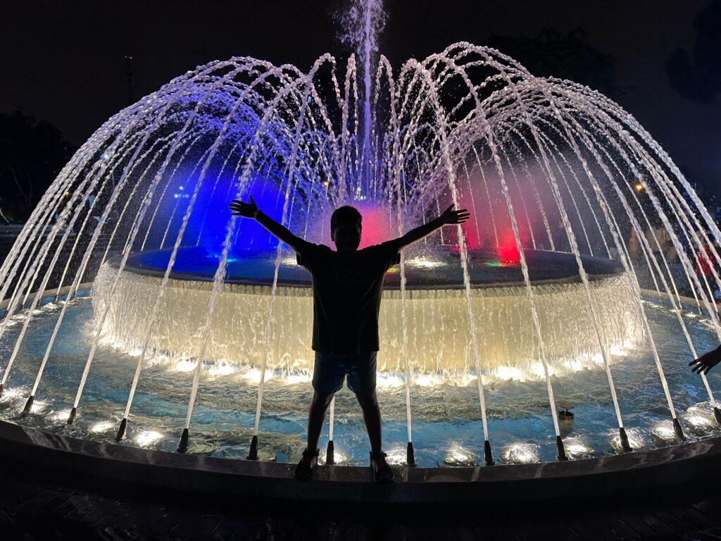 Kid in front of a fountain illuminated at night
